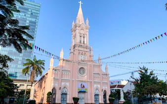 Pink Gothic-style cathedral in Da Nang with colorful flags and palm trees.