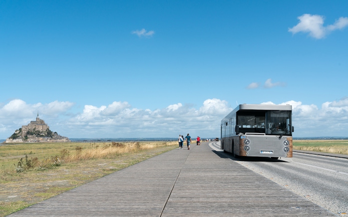 Tourist bus approaching Mont Saint-Michel, France, on a clear day.