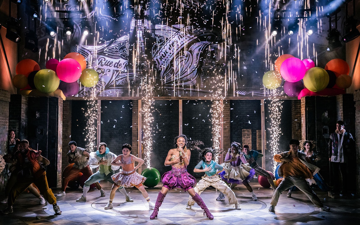 Performers dancing energetically on stage with colorful balloons and fireworks in "& Juliet" musical.