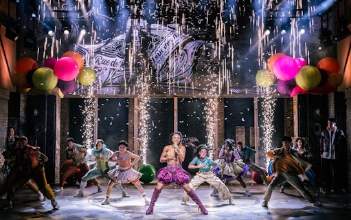 Performers dancing energetically on stage with colorful balloons and fireworks in "& Juliet" musical.