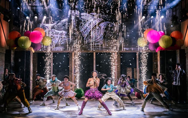 Performers dancing energetically on stage with colorful balloons and fireworks in "& Juliet" musical.