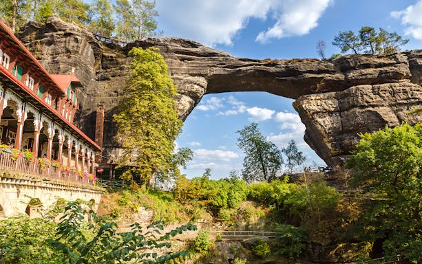 Pravcicka Brana rock arch with nearby historic building in Czech Republic.