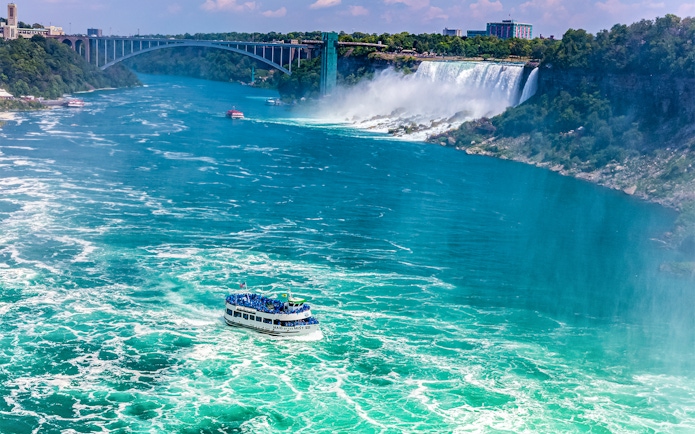 Maid of the Mist boat approaching Niagara Falls with Rainbow Bridge in the background.