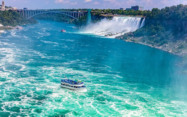 Maid of the Mist boat approaching Niagara Falls with Rainbow Bridge in the background.