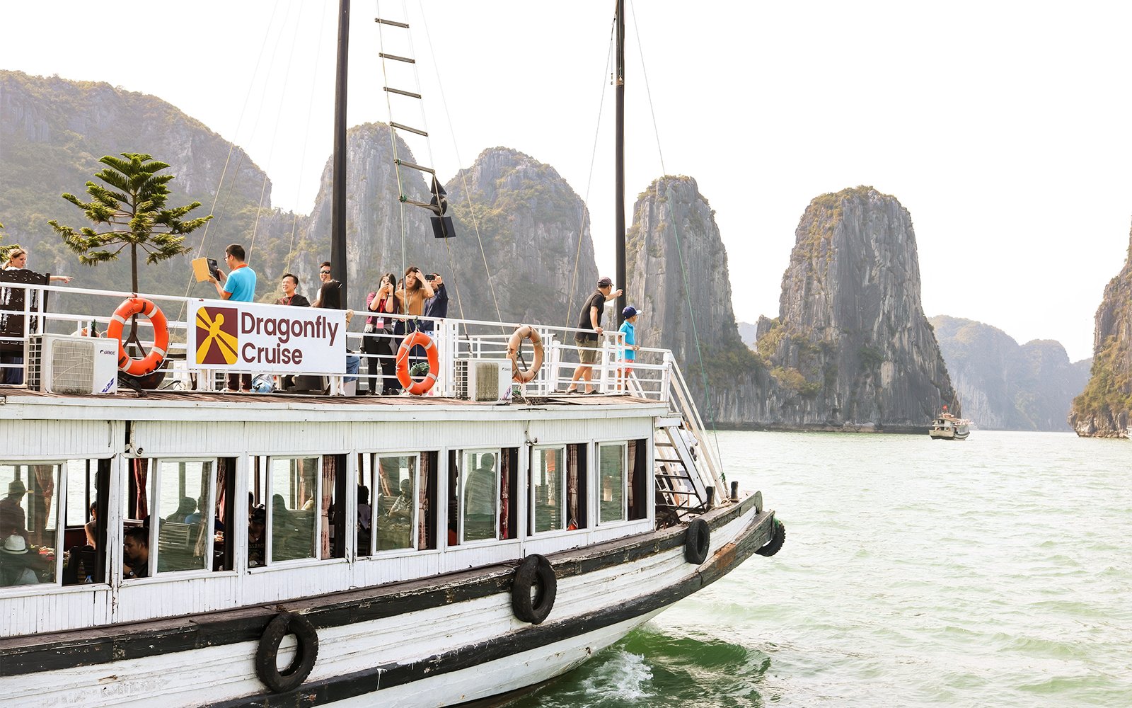 Dragonfly Standard Cruise boat with tourists in Ha Long Bay, Vietnam, limestone karsts in background.