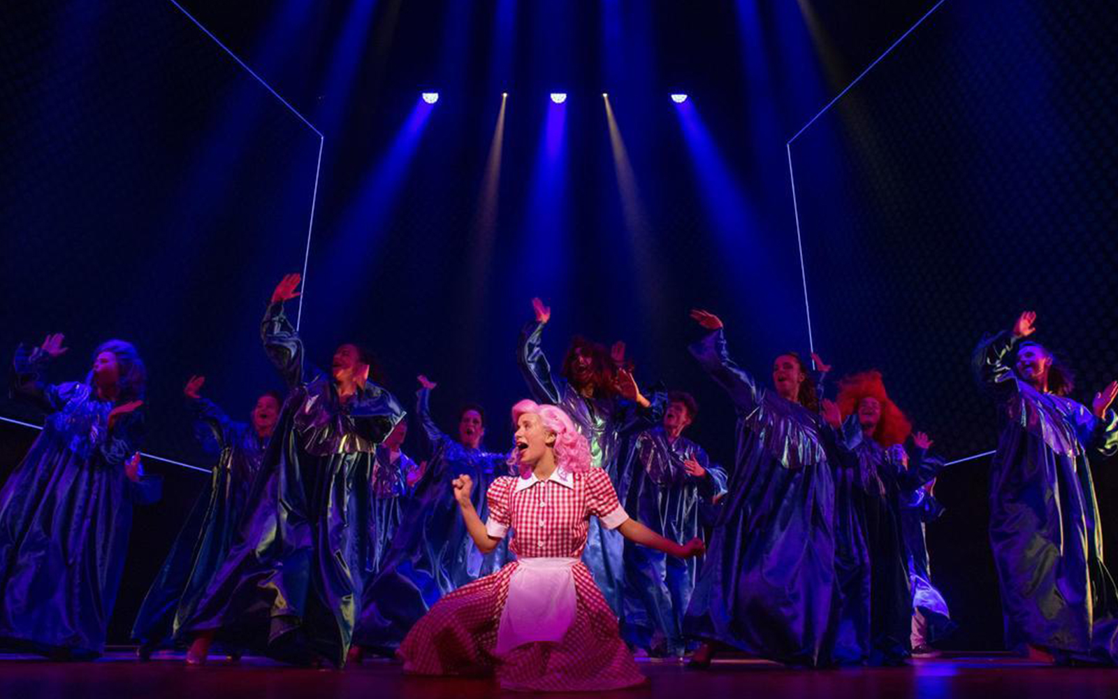 Performers in blue costumes dance on stage during a Grease musical scene.