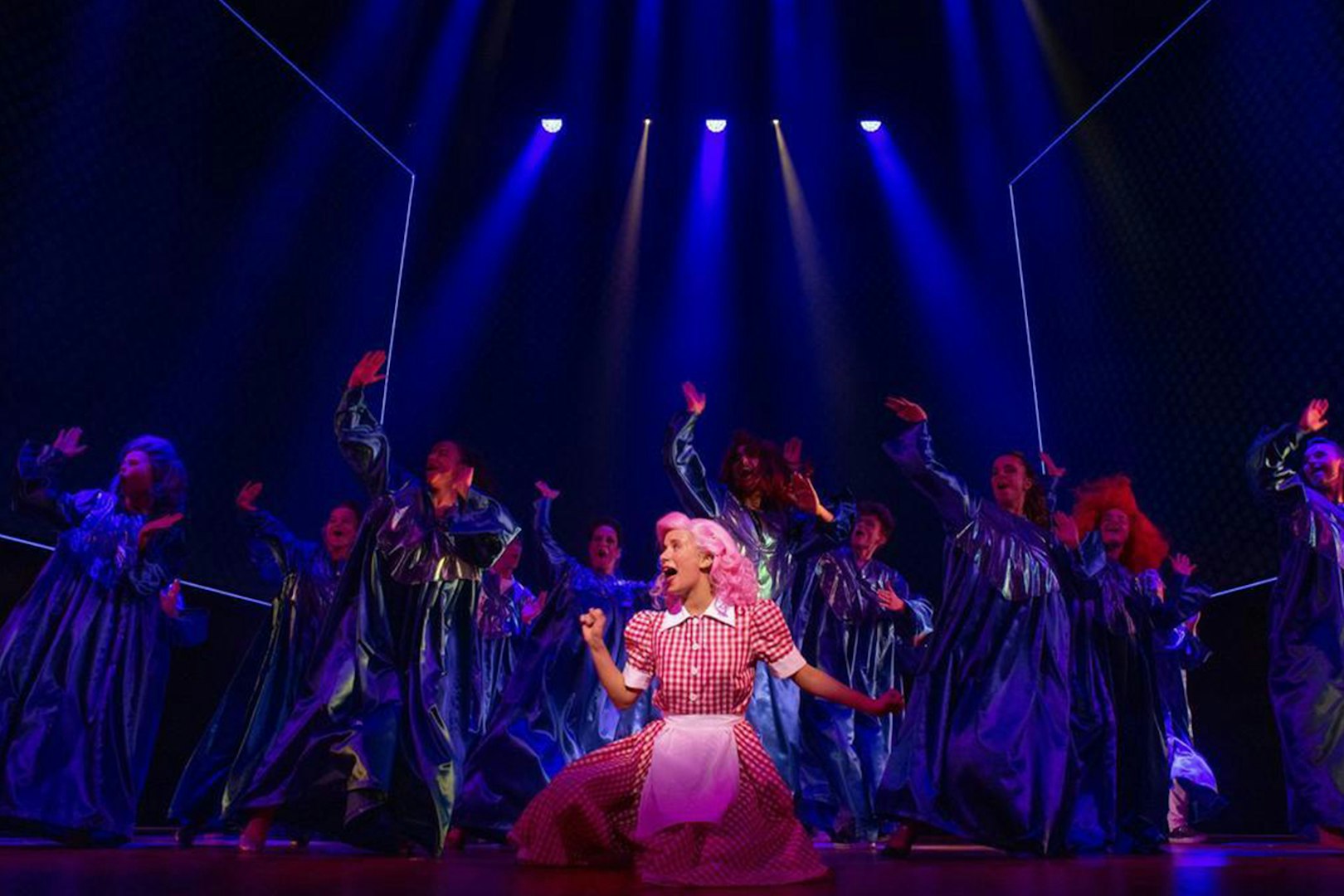 Performers in blue costumes dance on stage during a Grease musical scene.