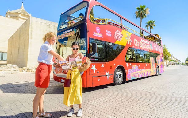 Woman with a passenger in front of a red hop-on hop-off sightseeing bus holding a map.