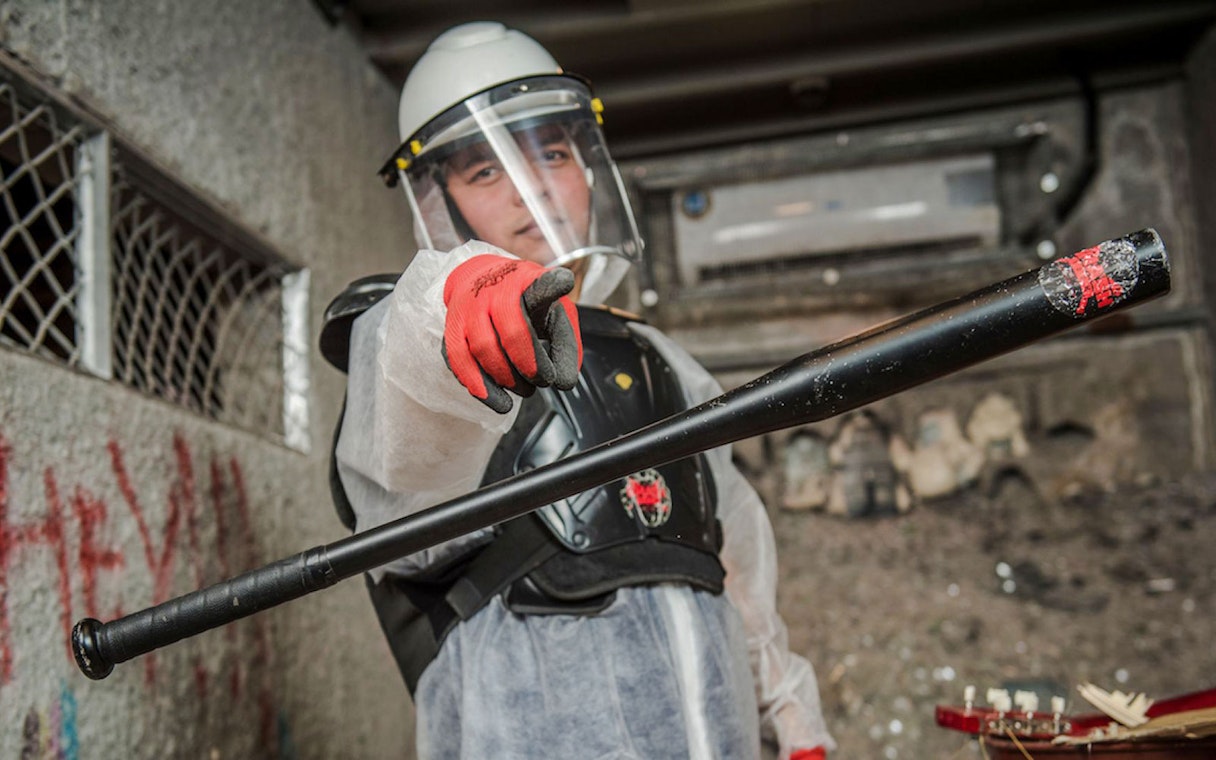 Visitor in protective gear holding a bat in a smash room.