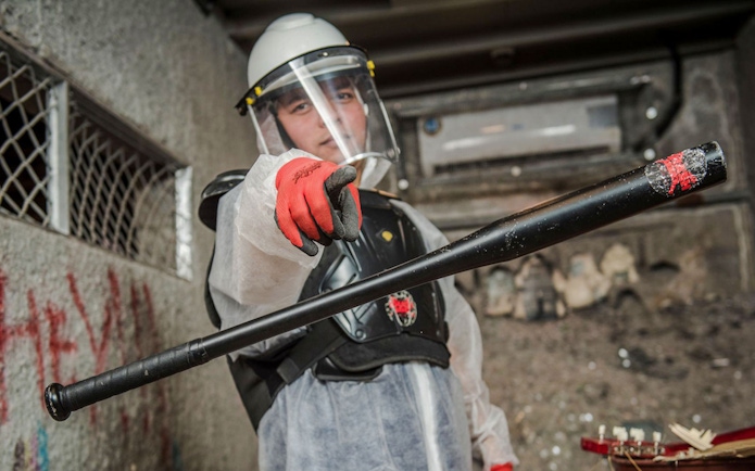 Visitor in protective gear holding a bat in a smash room.