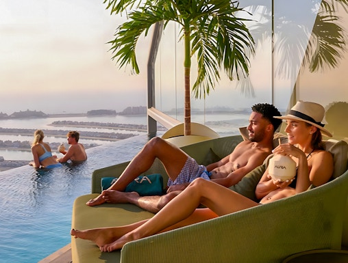 Couples relaxing at AURA Sky Pool, Dubai, with sunrise view over the city.