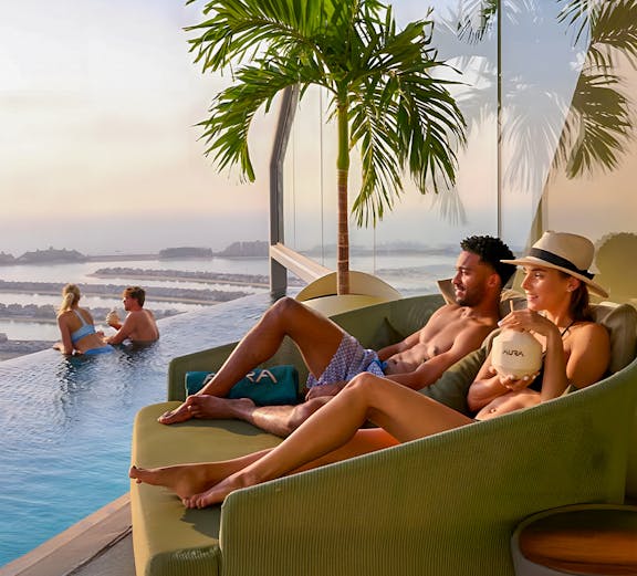 Couples relaxing at AURA Sky Pool, Dubai, with sunrise view over the city.