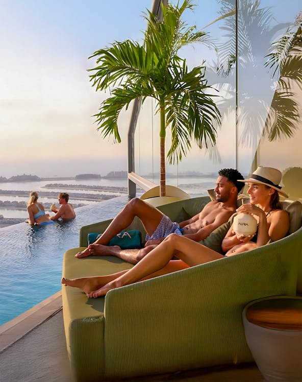 Couples relaxing at AURA Sky Pool, Dubai, with sunrise view over the city.
