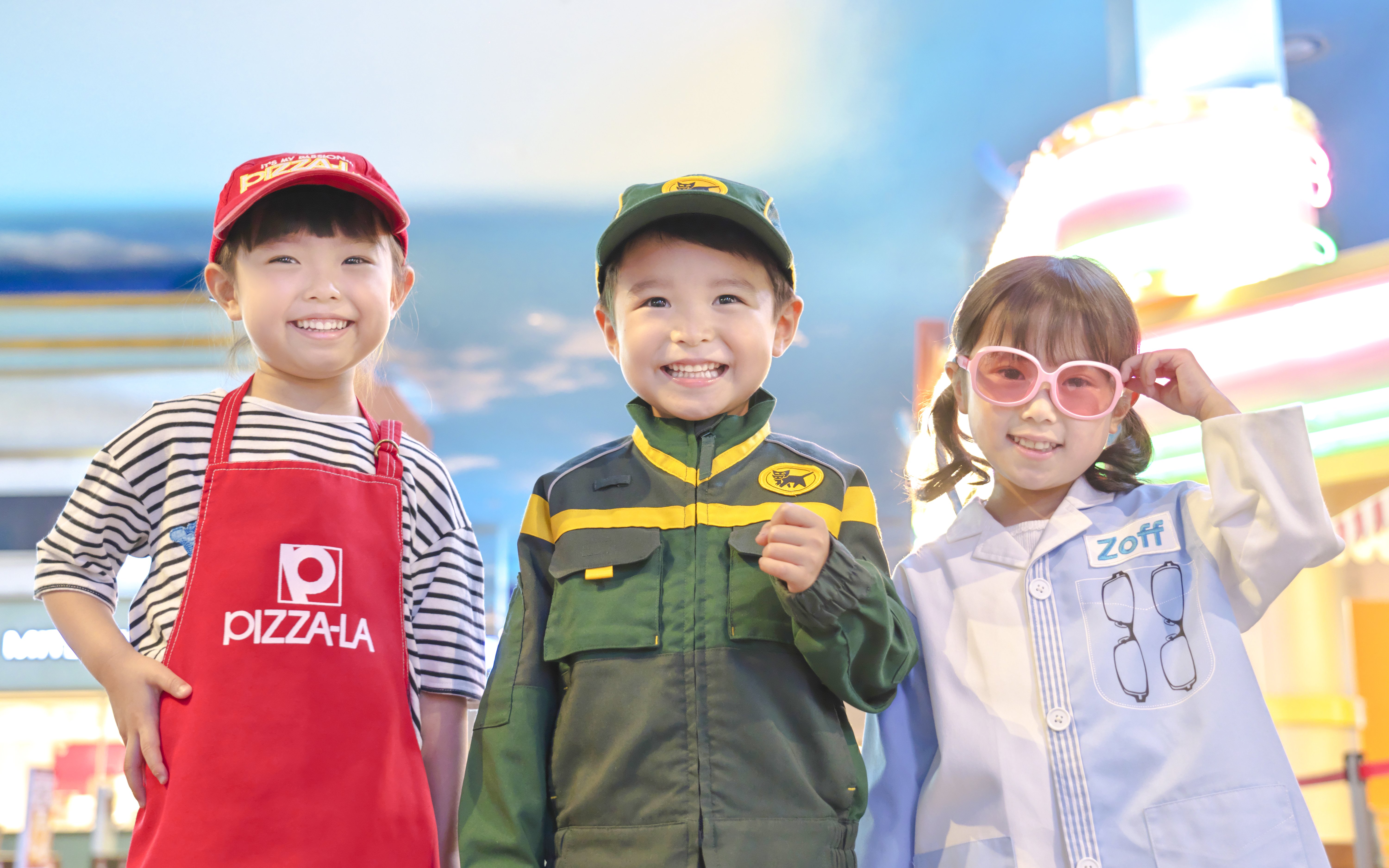 Children in themed costumes at KidZania Tokyo, including a pizza chef, delivery worker, and optician.