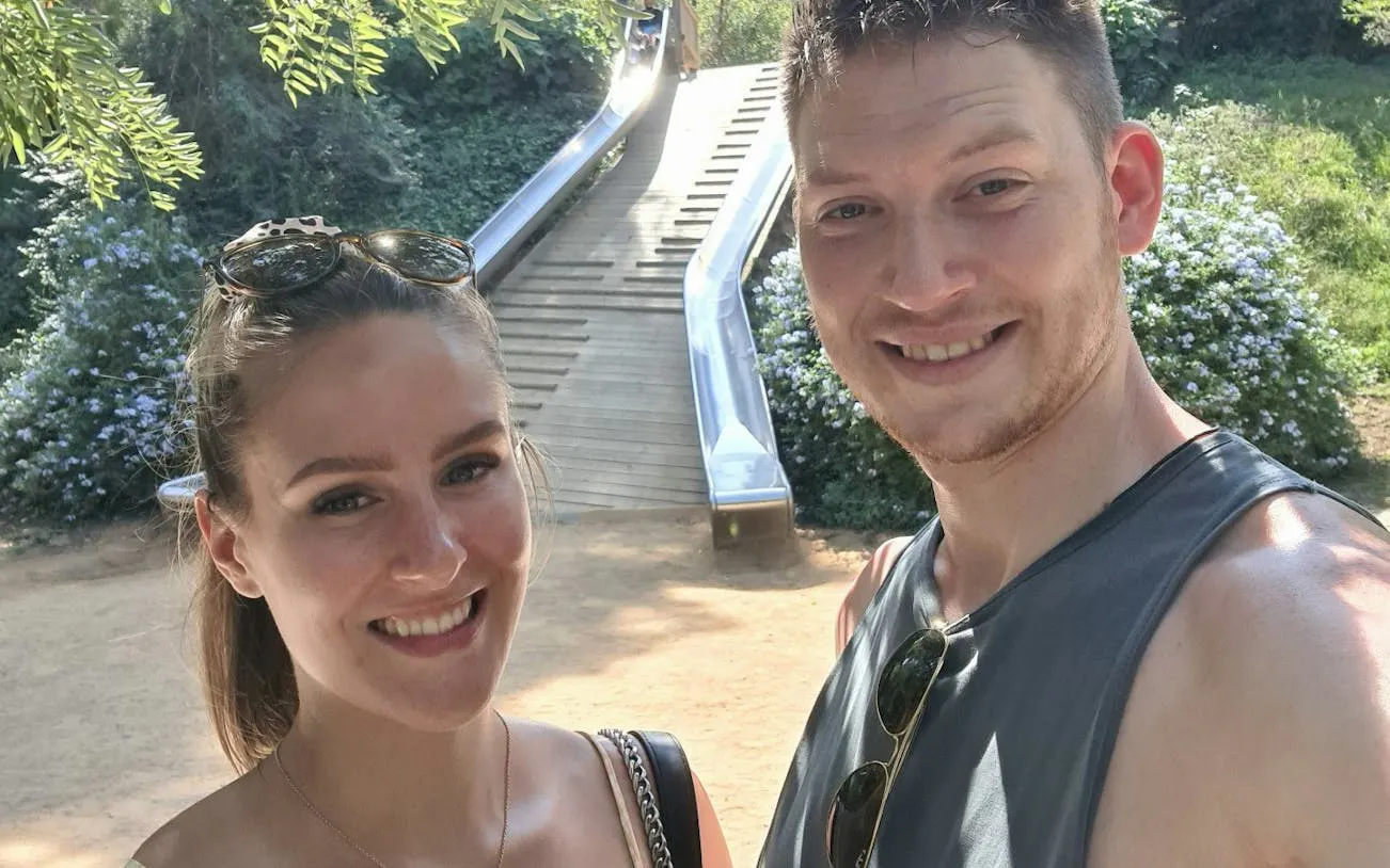 Couple enjoying a sunny day at a park in Barcelona with a slide in the background.