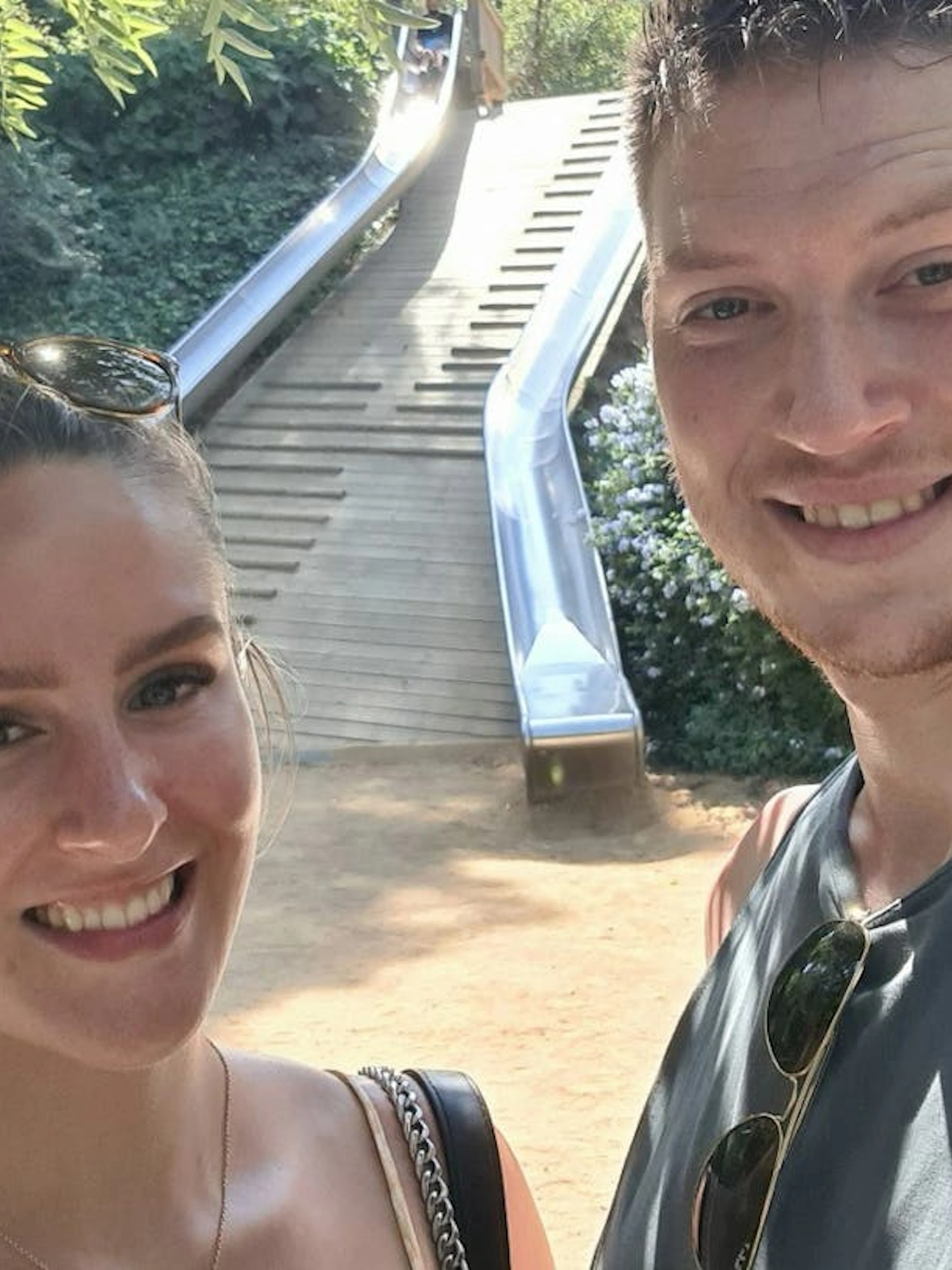 Couple enjoying a sunny day at a park in Barcelona with a slide in the background.
