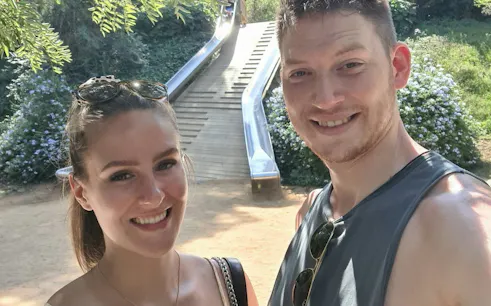 Couple enjoying a sunny day at a park in Barcelona with a slide in the background.