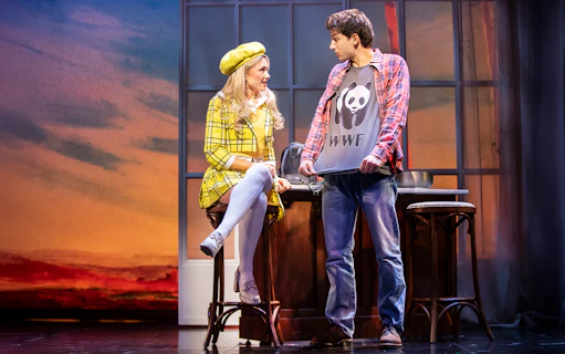 Two actors on stage in Clueless The Musical, one in a yellow plaid outfit, the other in a panda shirt.