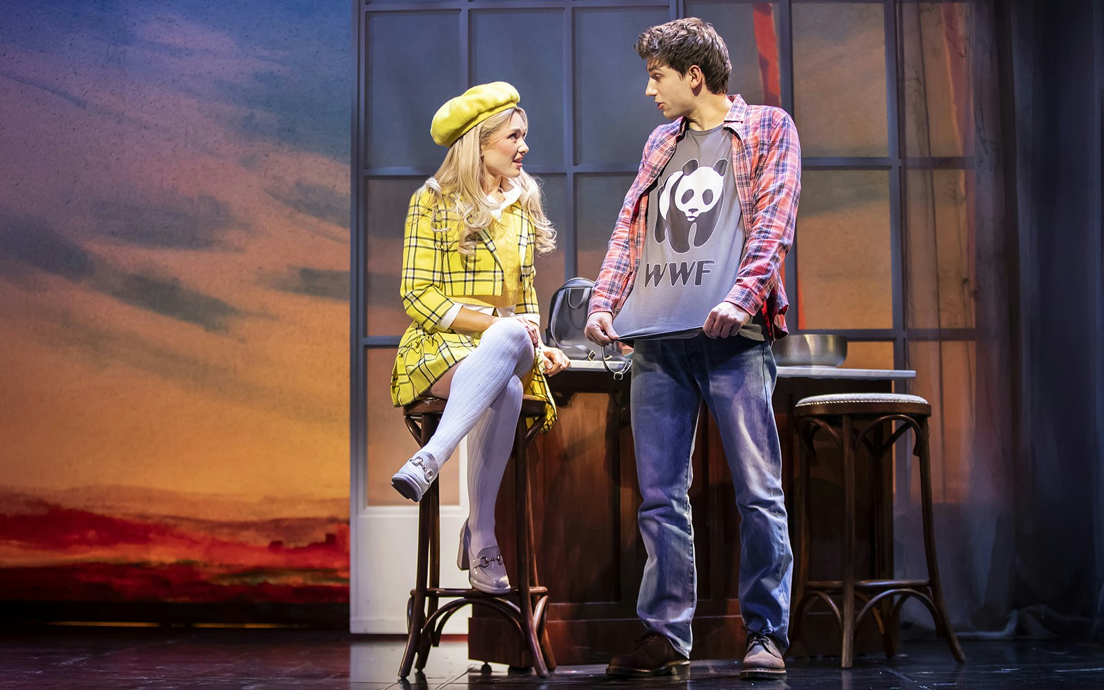 Two actors on stage in Clueless The Musical, one in a yellow plaid outfit, the other in a panda shirt.