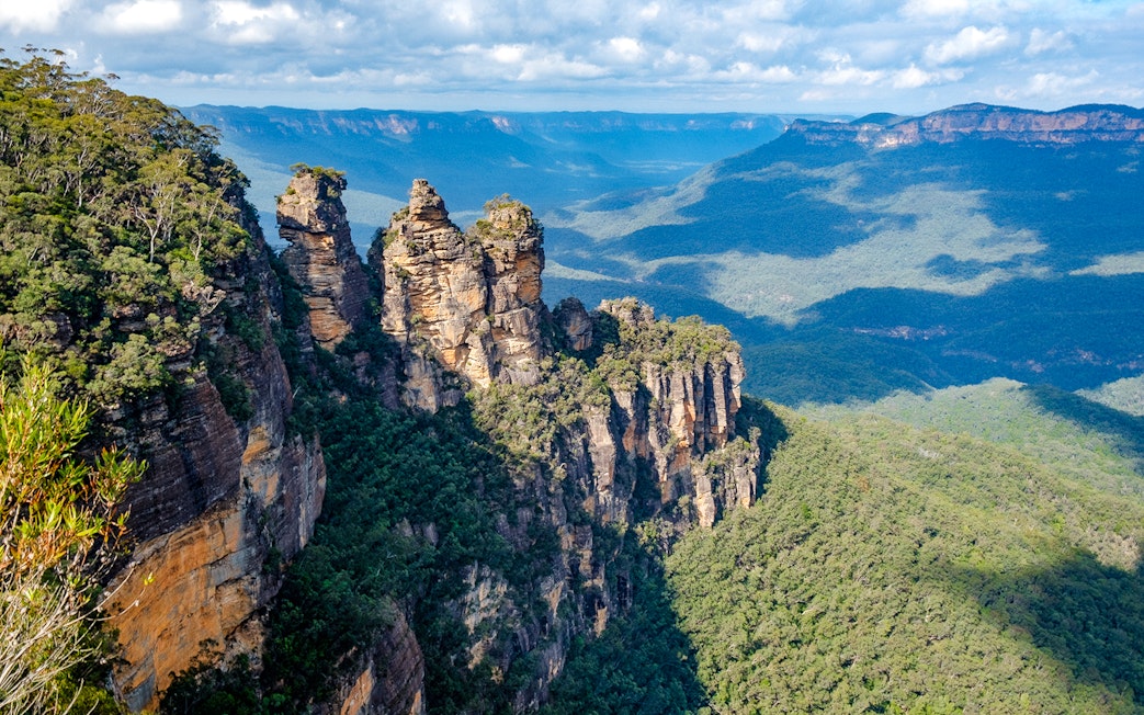 Three Sisters rock formation in Blue Mountains, Australia, surrounded by forest.