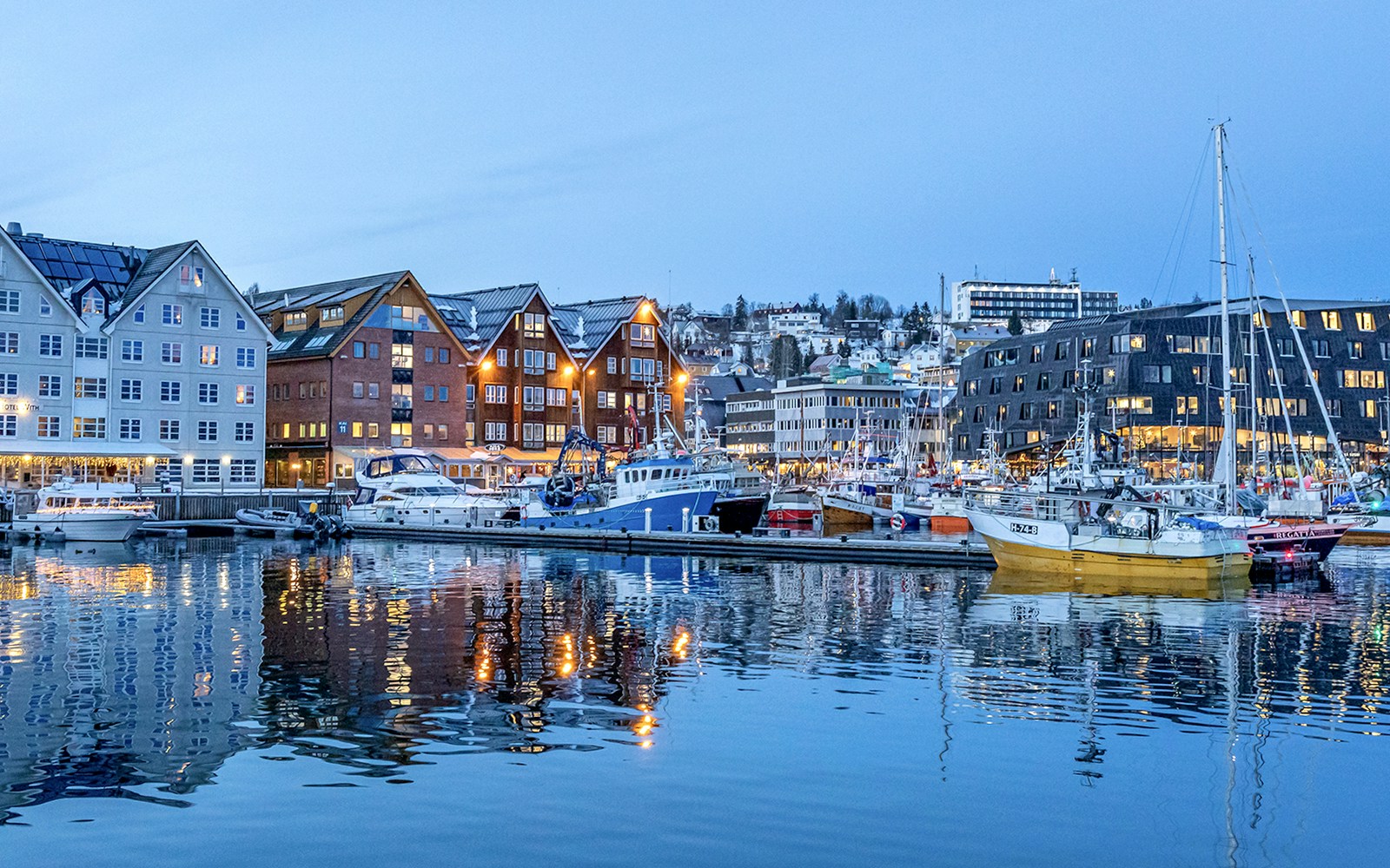 Tromso Harbor with snow-covered buildings and boats, surrounded by mountains.