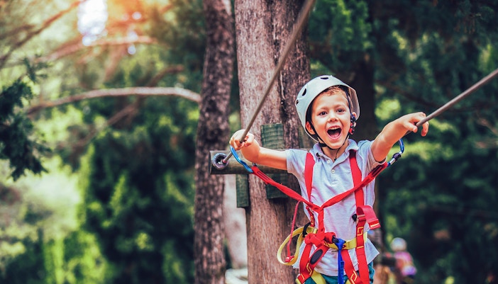 Little boy with helmet and safety equipment climbing a tree in an adventure activity park