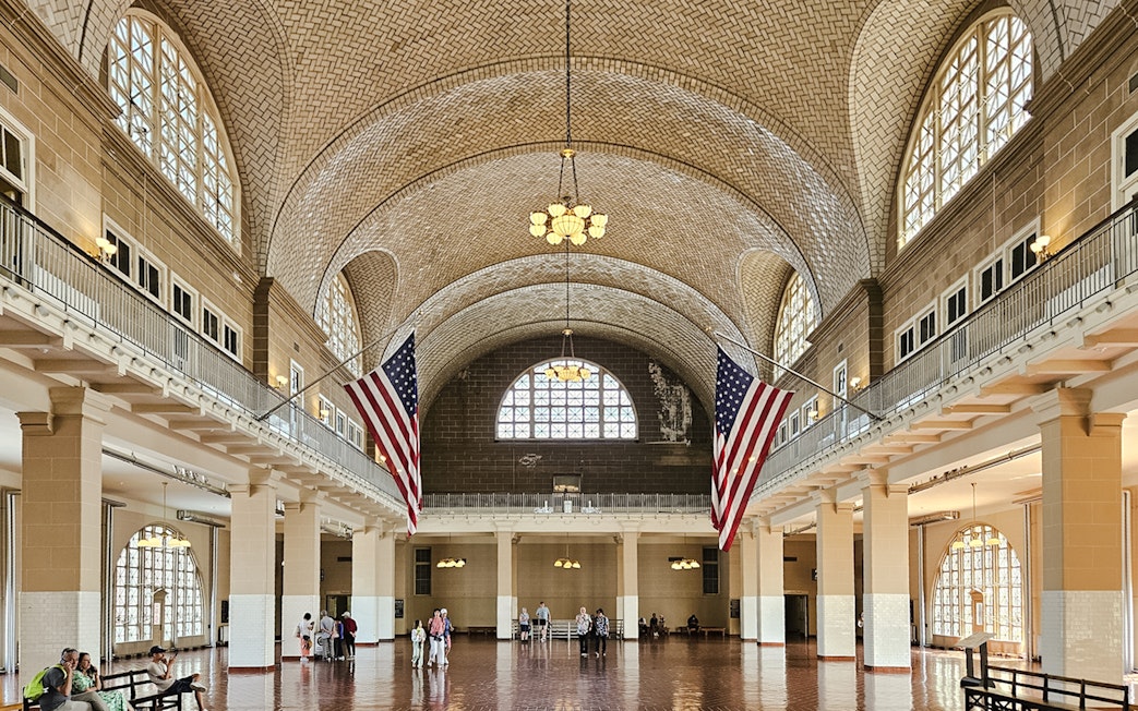 Wide-angle view of the Great Hall interior at Ellis Island National Museum of Immigration, featuring American flags.