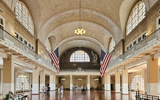 Wide-angle view of the Great Hall interior at Ellis Island National Museum of Immigration, featuring American flags.