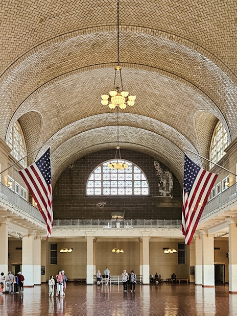 Wide-angle view of the Great Hall interior at Ellis Island National Museum of Immigration, featuring American flags.