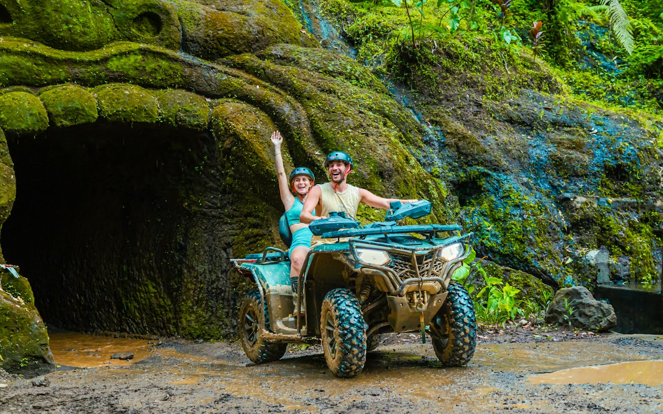Couple riding ATV near cave entrance in Ubud jungle.