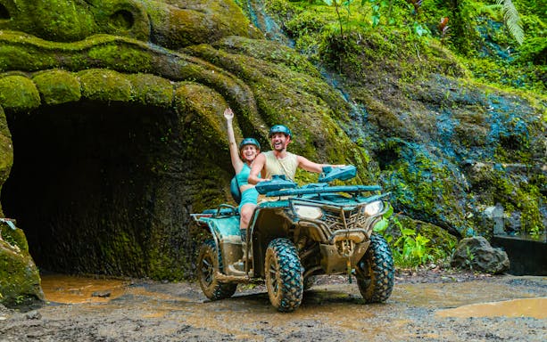 Couple riding ATV near cave entrance in Ubud jungle.