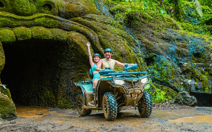 Couple riding ATV near cave entrance in Ubud jungle.