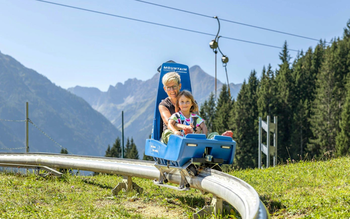 Family enjoying mountain coaster ride in Gabala with scenic forest and mountain views.