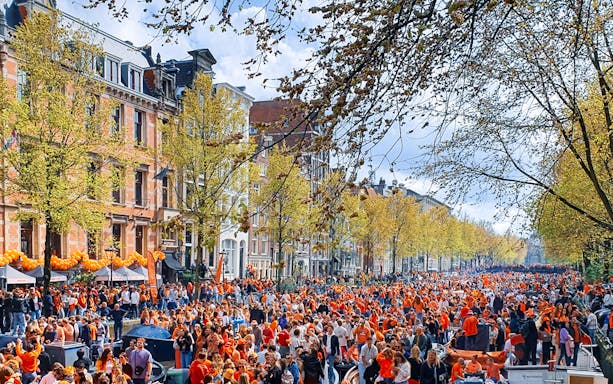 Crowd celebrating King's Day on a canal in Amsterdam with orange decorations.