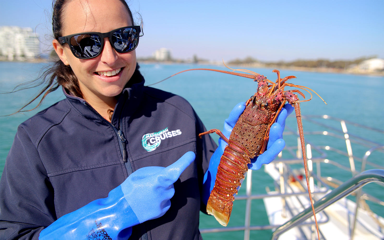 Woman on a boat holding a large lobster in gloved hands.