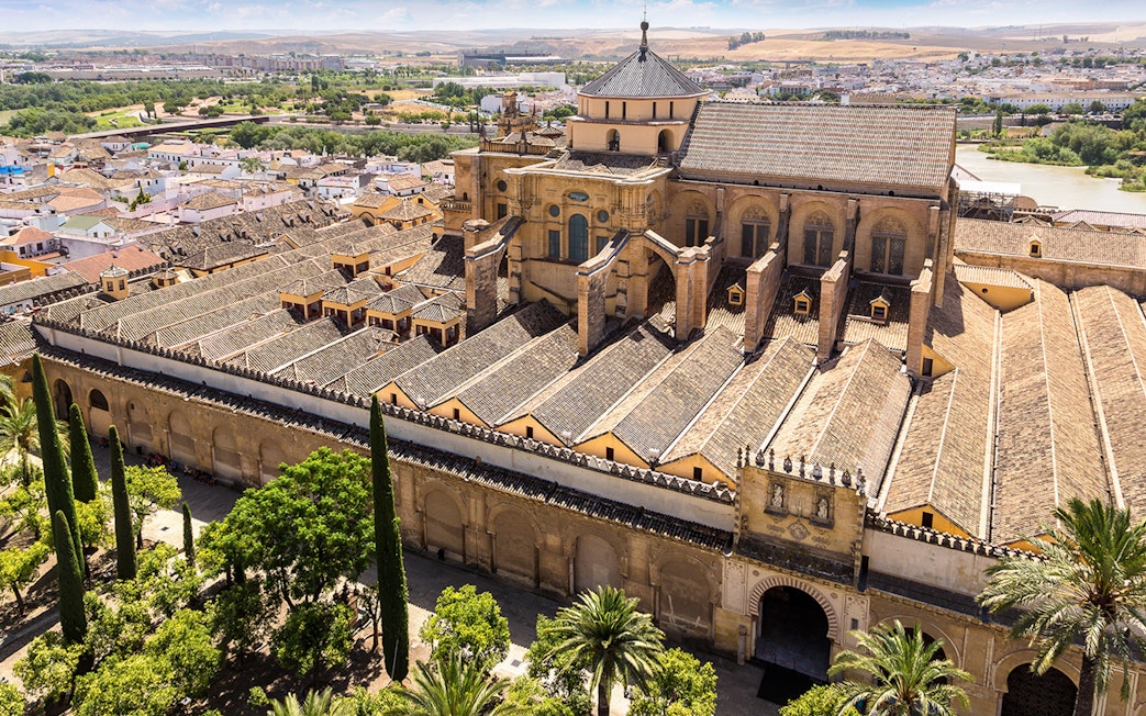 Aerial view of the historic Mosque-Cathedral in Córdoba, Spain, surrounded by lush gardens.