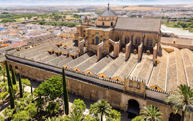 Aerial view of the historic Mosque-Cathedral in Córdoba, Spain, surrounded by lush gardens.