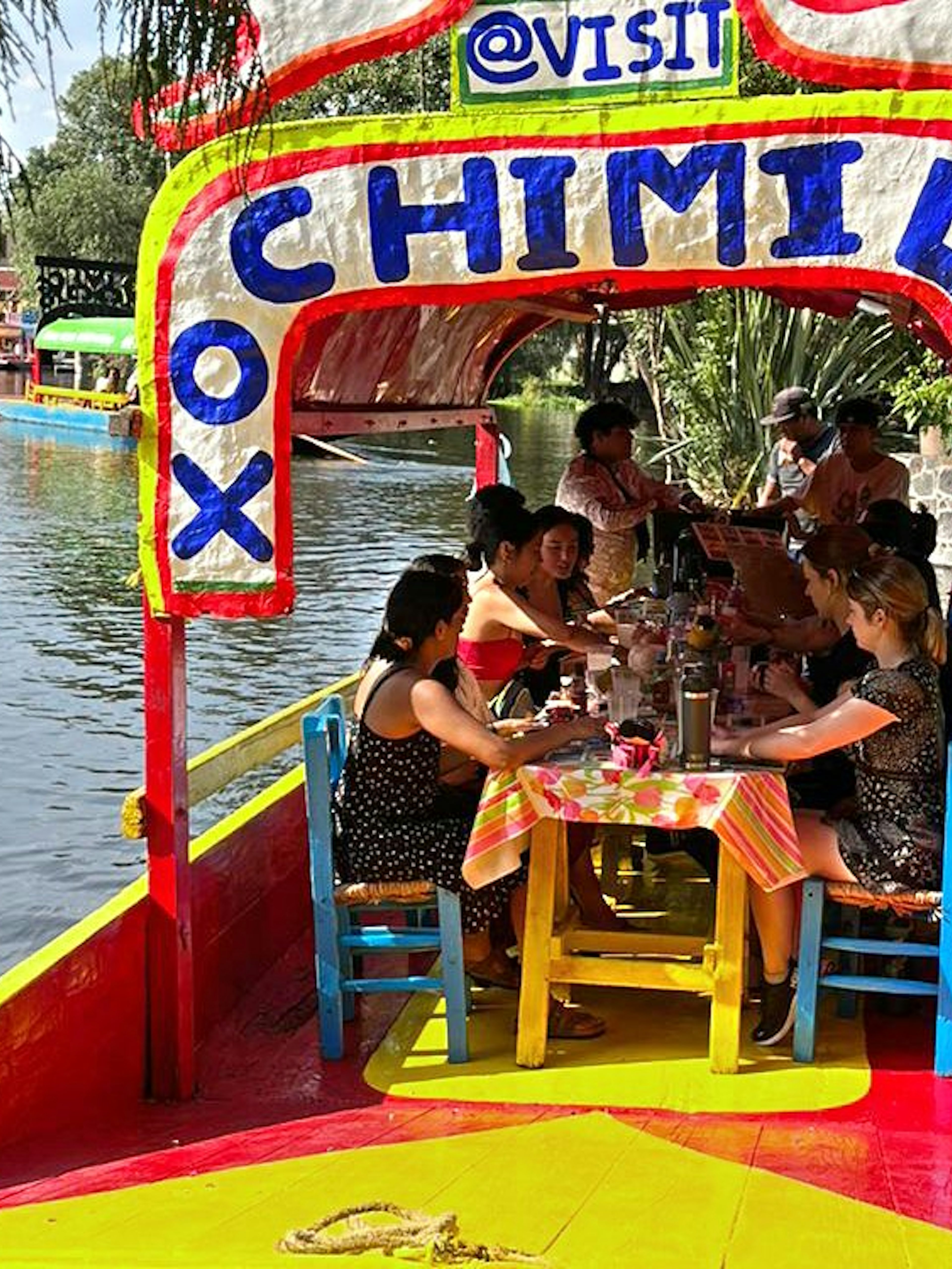 Trajinera boat with people enjoying drinks on Xochimilco canals, Mexico City.