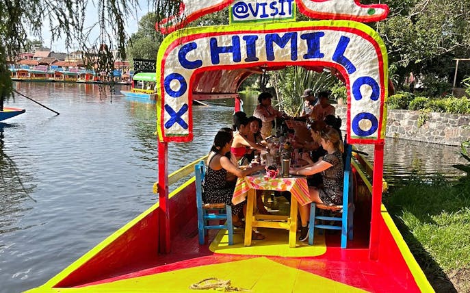 Trajinera boat with people enjoying drinks on Xochimilco canals, Mexico City.