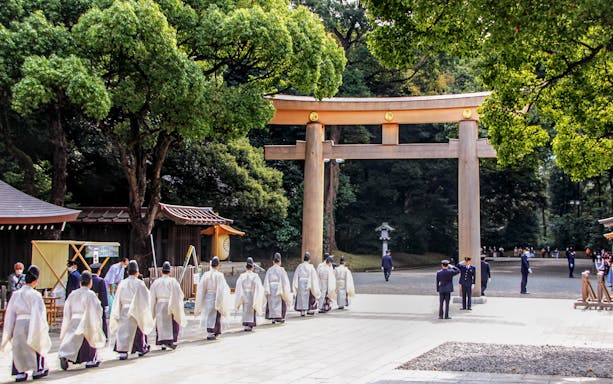 Priests in traditional attire walking under a torii gate at Meiji Shrine, Tokyo.
