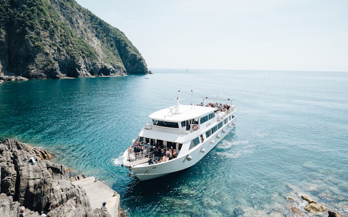 Boat arriving at rocky shore in Cinque Terre, Italy, with passengers on deck.