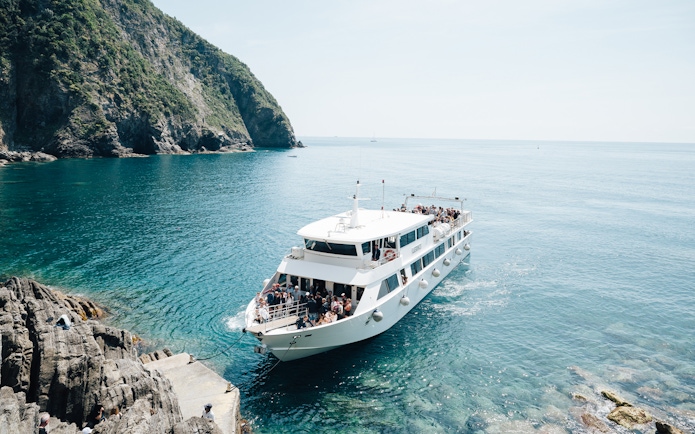 Boat arriving at rocky shore in Cinque Terre, Italy, with passengers on deck.