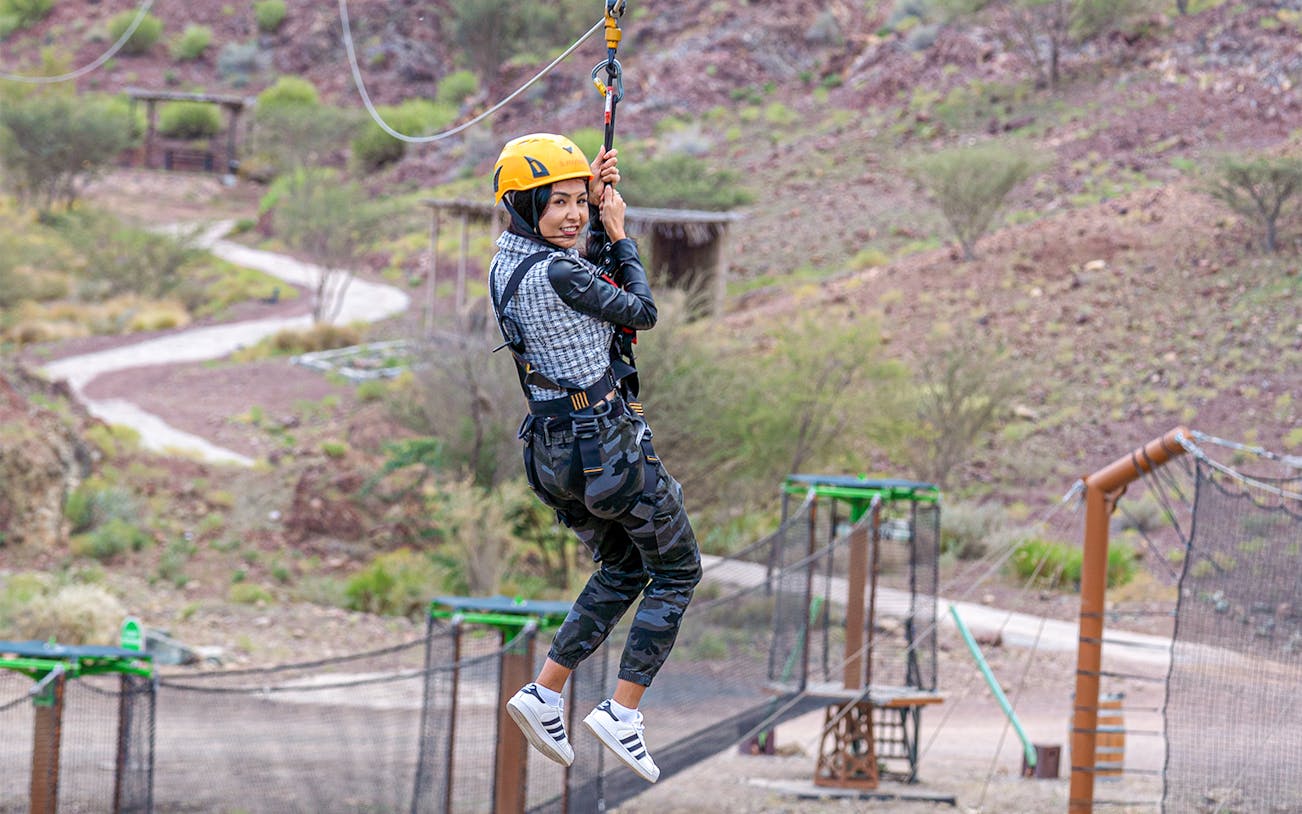 Person ziplining at Hatta Wadi Hub with desert landscape in background.
