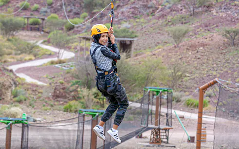 Person ziplining at Hatta Wadi Hub with desert landscape in background.