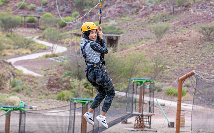 Person ziplining at Hatta Wadi Hub with desert landscape in background.