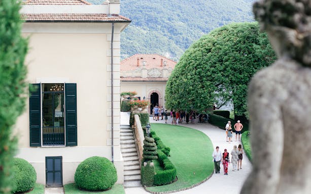 Villa Del Balbianello park with visitors walking along manicured paths and lush greenery.