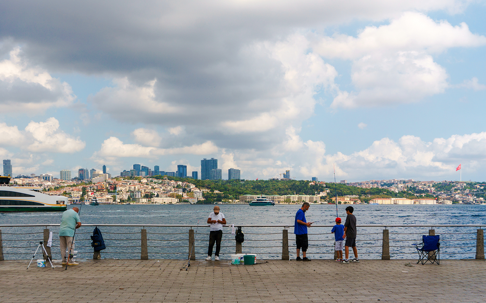 People fishing along the waterfront with the Istanbul skyline in the background.