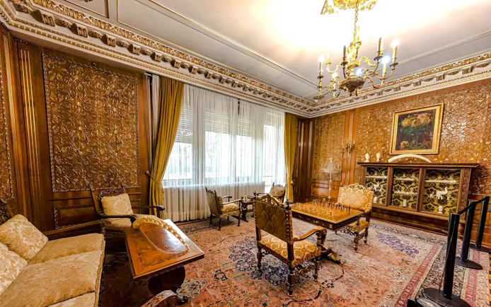 Luxurious room with ornate wood paneling and chandelier inside Ceausescu Mansion.