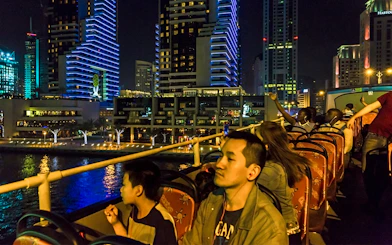 Open-top bus tour at night in Dubai Marina with illuminated skyscrapers.