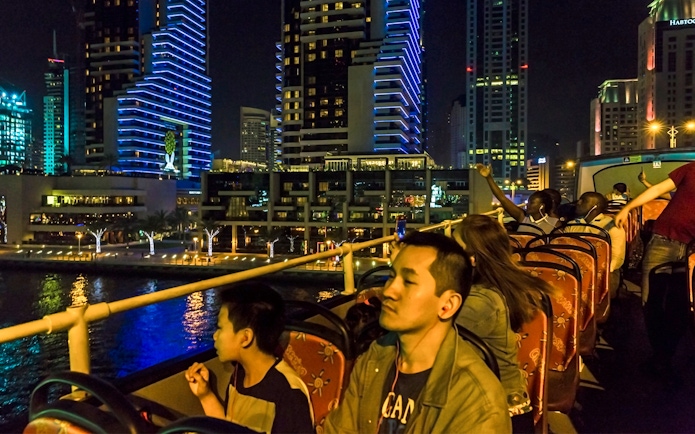 Open-top bus tour at night in Dubai Marina with illuminated skyscrapers.